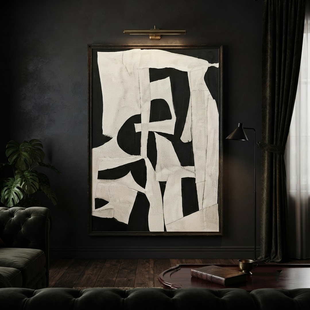 Abstract black and off-white geometric wall art hanging in a dark moody living room with a tufted sofa, floor lamp, and dark curtains.