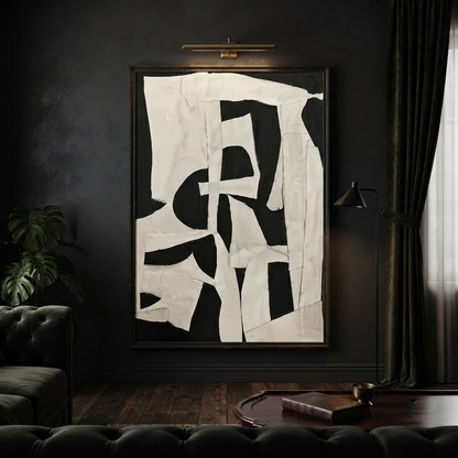 Abstract black and off-white geometric wall art hanging in a dark moody living room with a tufted sofa, floor lamp, and dark curtains.