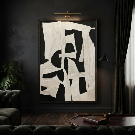 Abstract black and off-white geometric wall art hanging in a dark moody living room with a tufted sofa, floor lamp, and dark curtains.